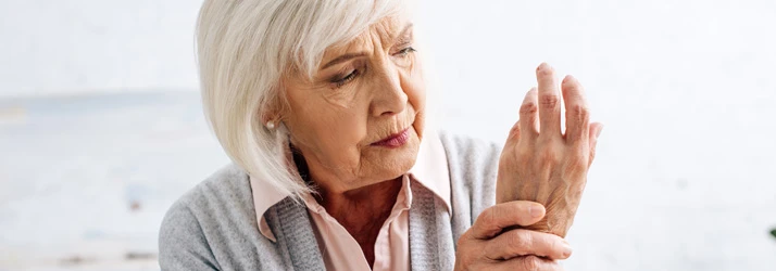 Adult holding the wrist with visible discomfort, representing wrist pain, joint strain, or arthritis concerns.